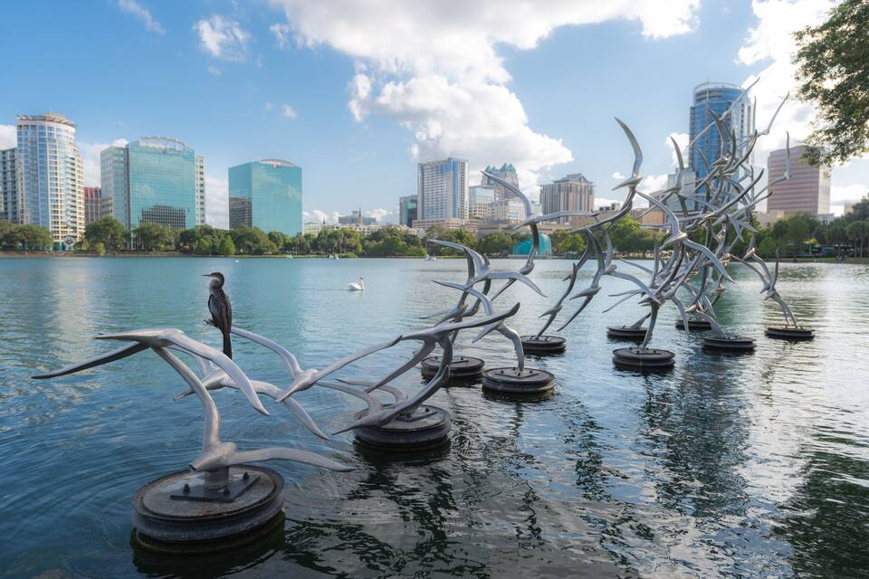 A lake with sculptures of birds and fish, surrounded by city buildings.
