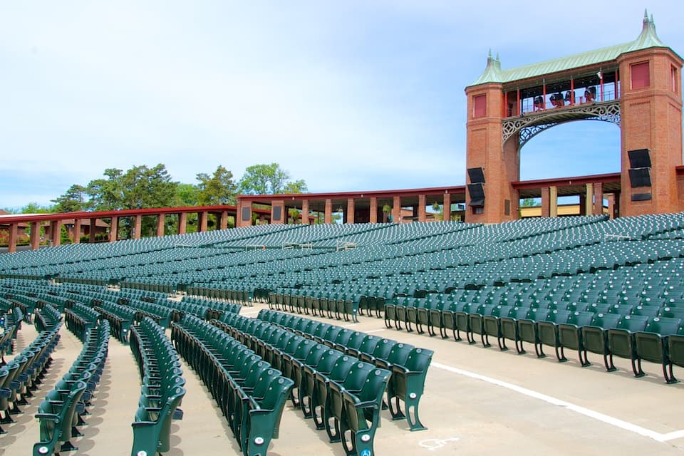 A large, empty stadium with rows of green seats and a prominent brick tower with a green roof.