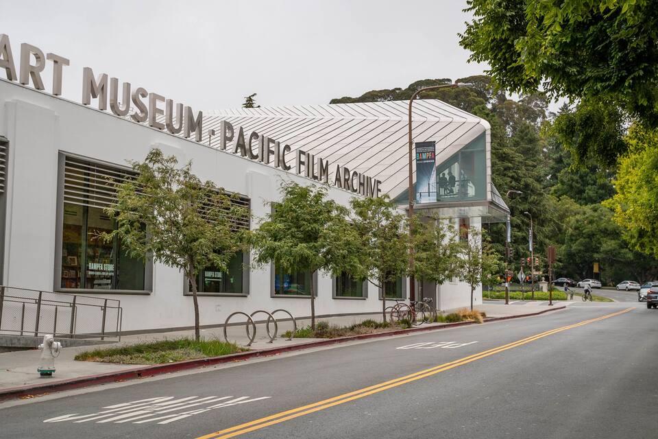 Edifício da Art Museum Pacific Film Archive com design moderno, janelas amplas e uma rua visível com carros e um ciclista.