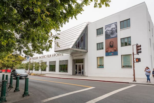 Kunstmuseet Pacific Film Archives bygning med et moderne design, beliggende i et gadehjørne med et lyskryds og fodgængere i nærheden.