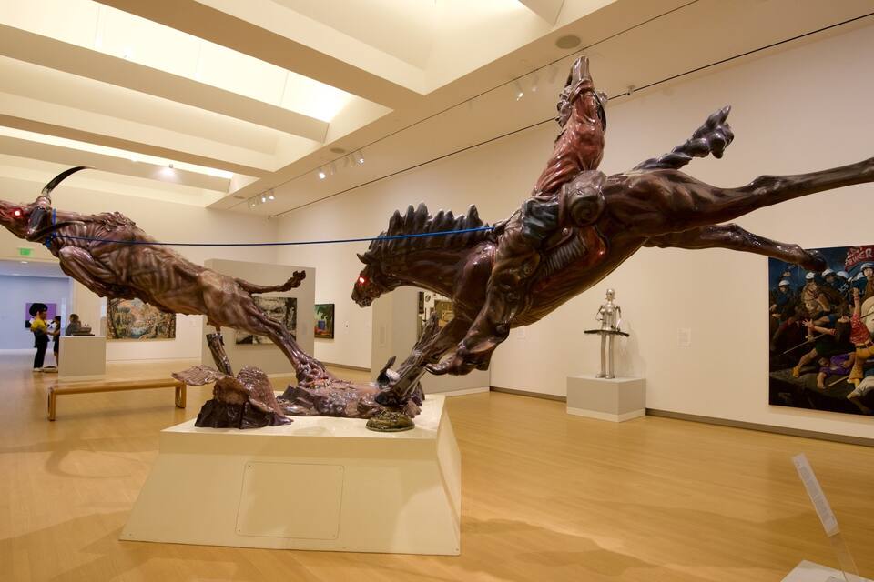 A museum interior with large sculptures of horses and a human figure on pedestals.