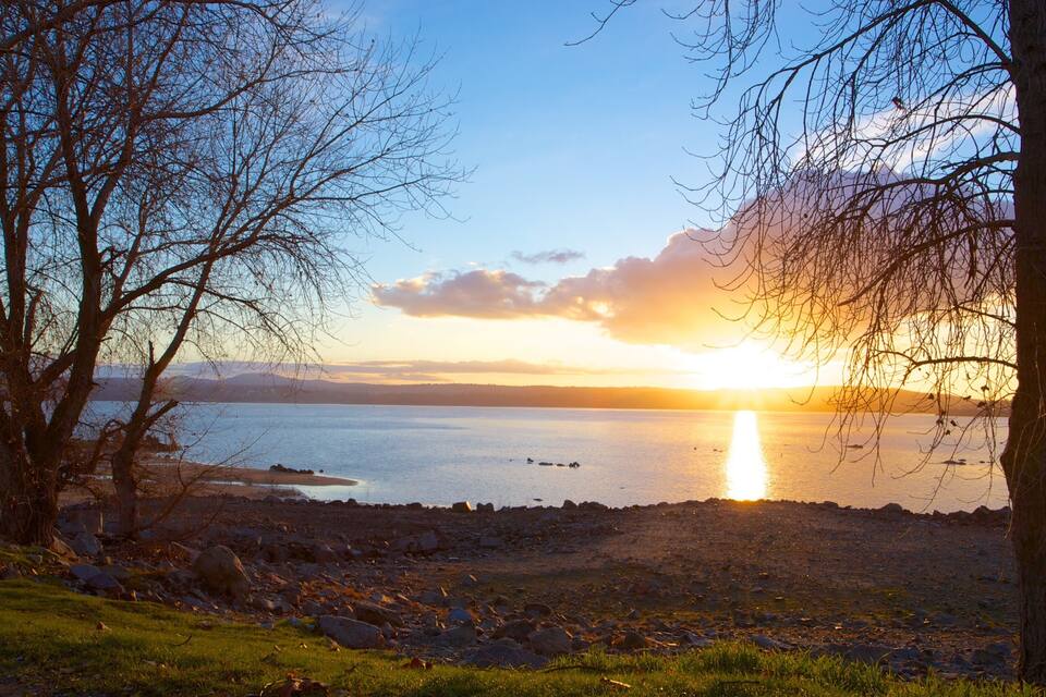 A sunset over a calm lake with rocky shores and leafless trees.