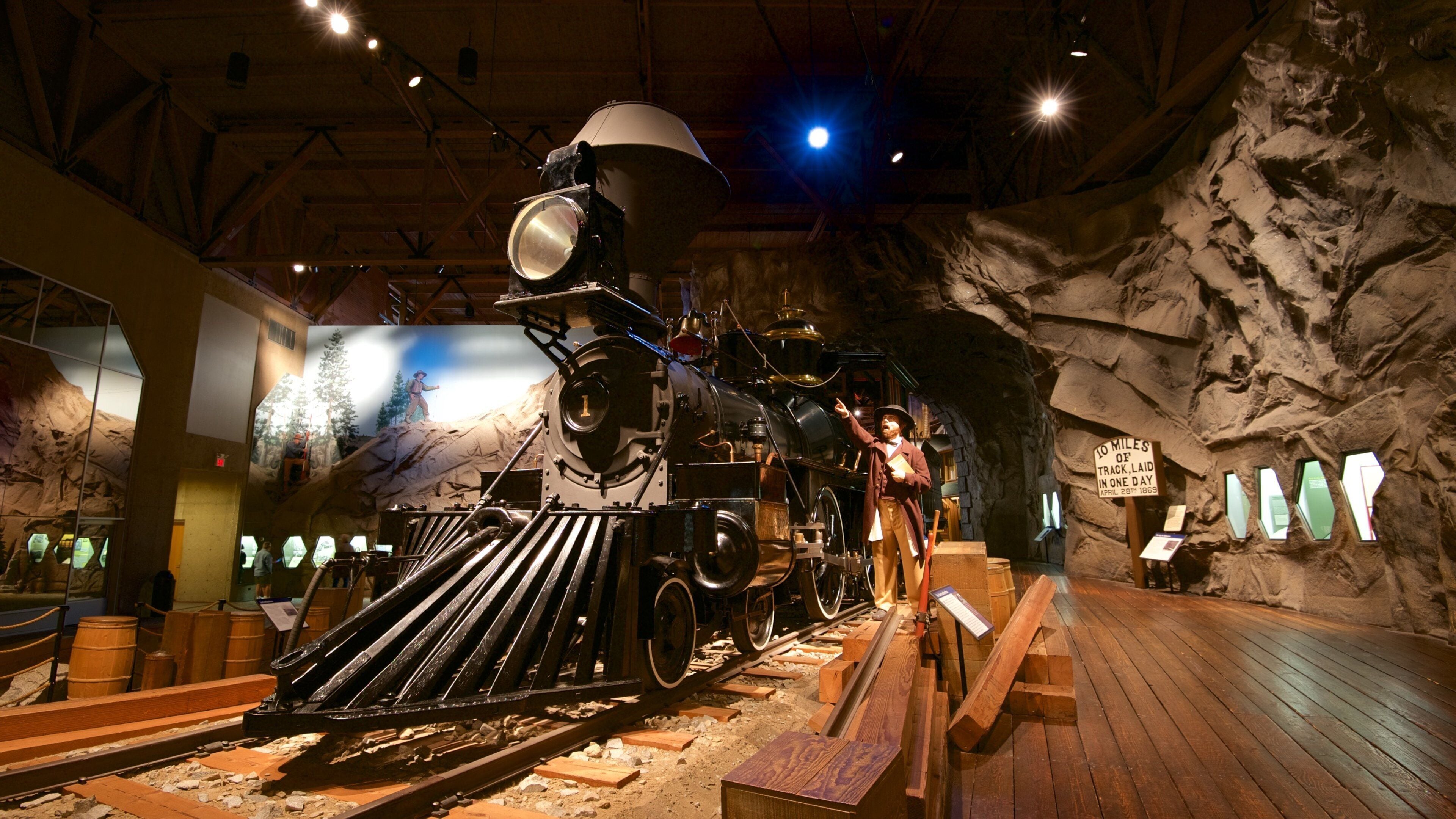 A steam locomotive in a museum exhibit with a rocky backdrop and a sign indicating a historical achievement.