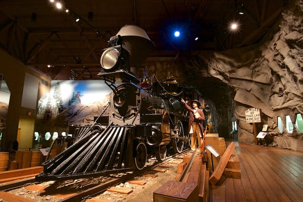 A steam locomotive in a museum exhibit with a rocky backdrop and a sign indicating a historical achievement.