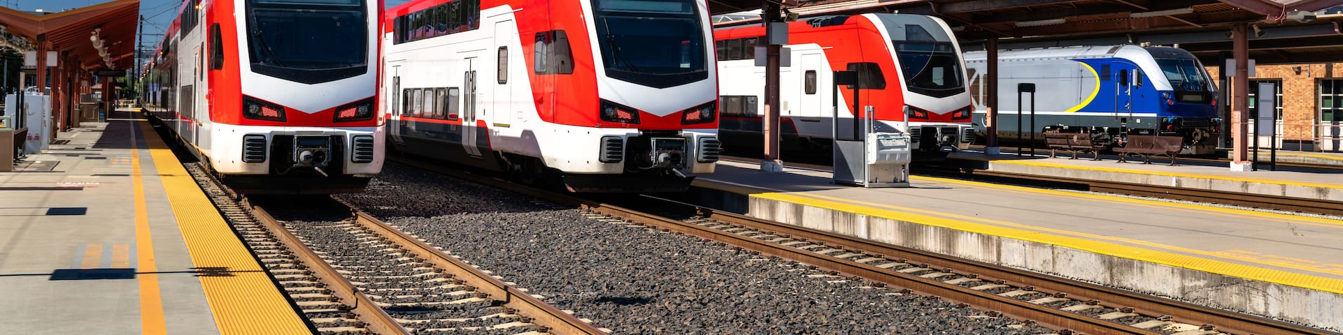 A train station with three trains on the tracks and a blue train in the background.