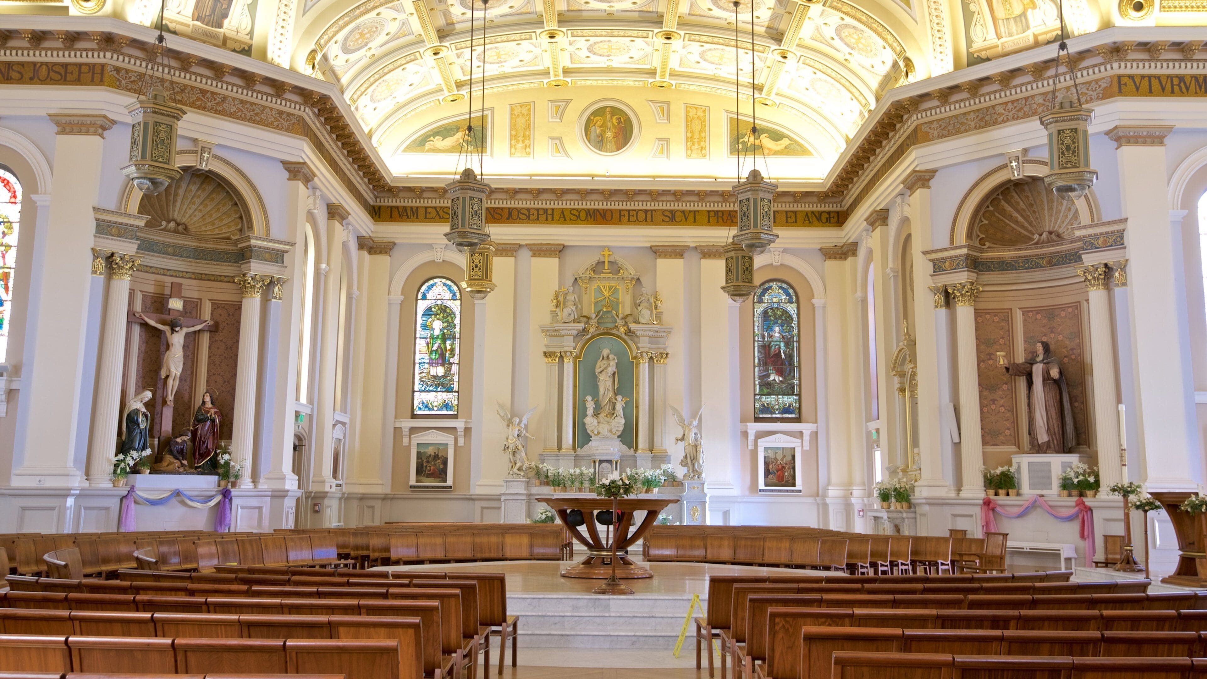 Interior de igreja ricamente decorado, com teto alto, vitrais e estátuas religiosas.
