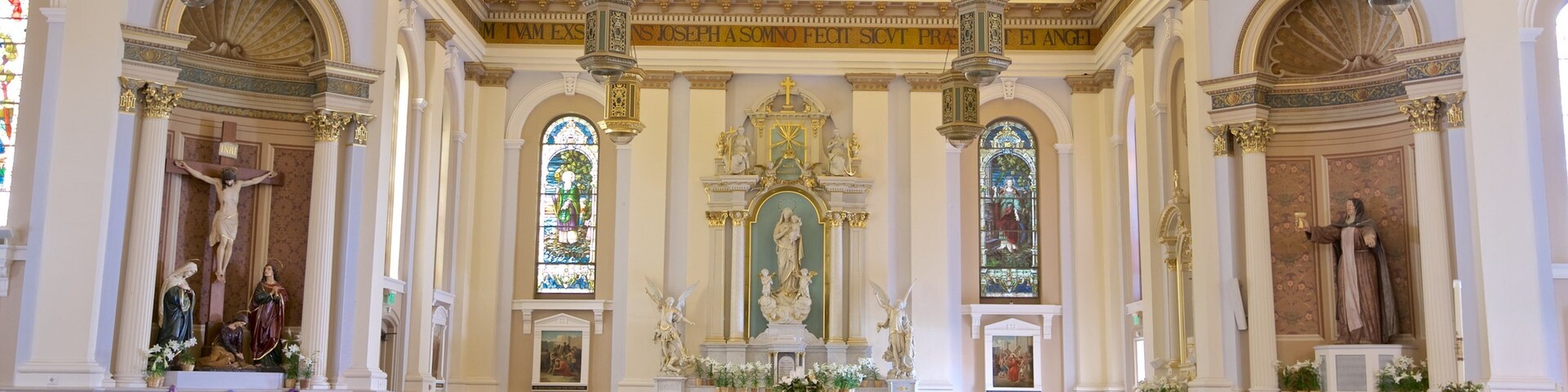 Interior de igreja ricamente decorado, com teto alto, vitrais e estátuas religiosas.