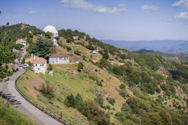 Une route sinueuse sur une colline, avec une grande structure en forme de dôme blanc et des immeubles résidentiels.