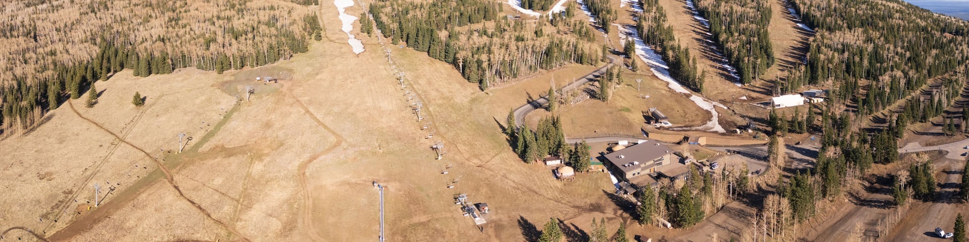 Panoramic view of Arizona snowbowl ski resort near Flagstaff, USA, suffering from unusual lack of snow in early april 2026, due to climate change. Aerial view, late afternoon.