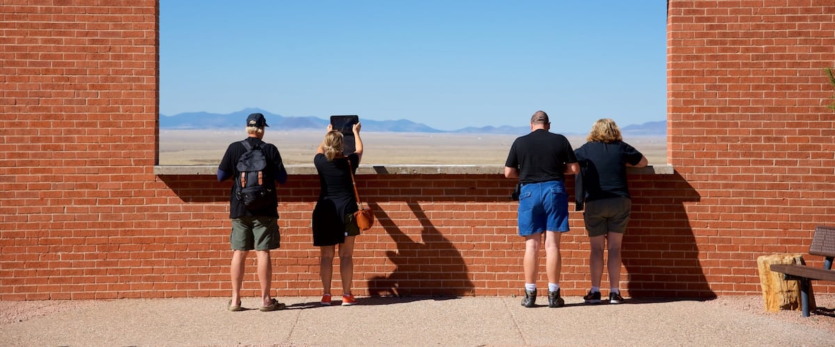 Four people standing in front of a large mural of a desert landscape with mountains in the distance.