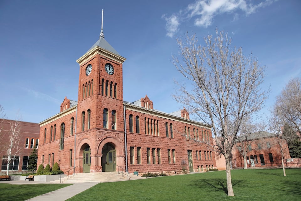 A large brick building with a clock tower, green lawn, and leafless trees.