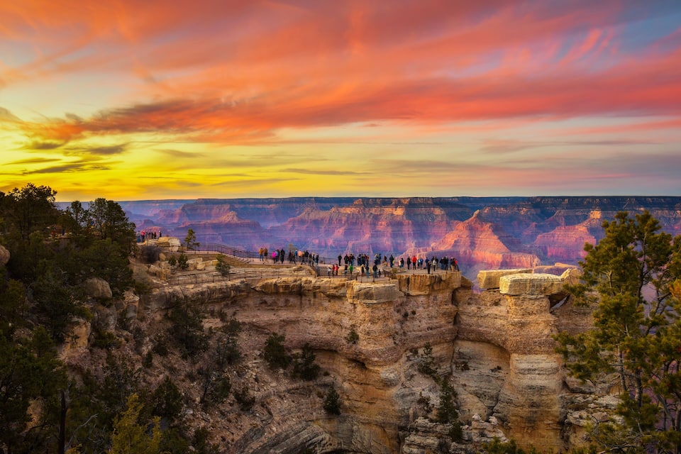 A canyon with a sunset sky, a viewing platform with people, and rocky cliffs.