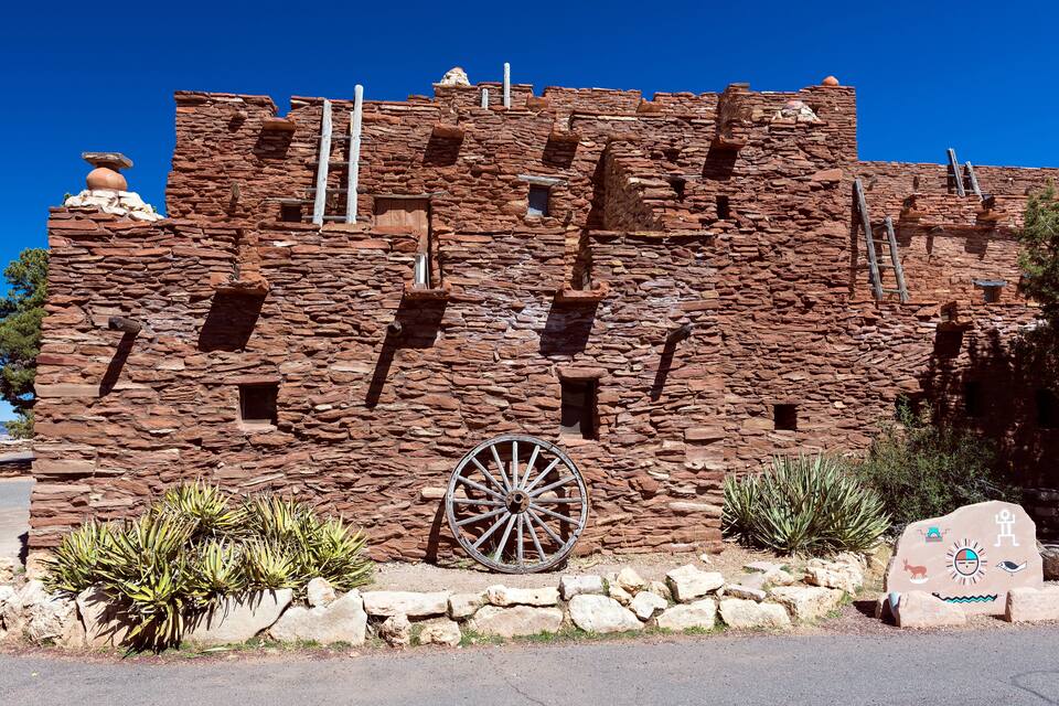 A historic stone building with a large wheel and native plants.