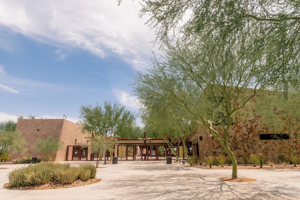 A building labeled "Home Plate Gate" with a stone wall and a tree in the foreground.