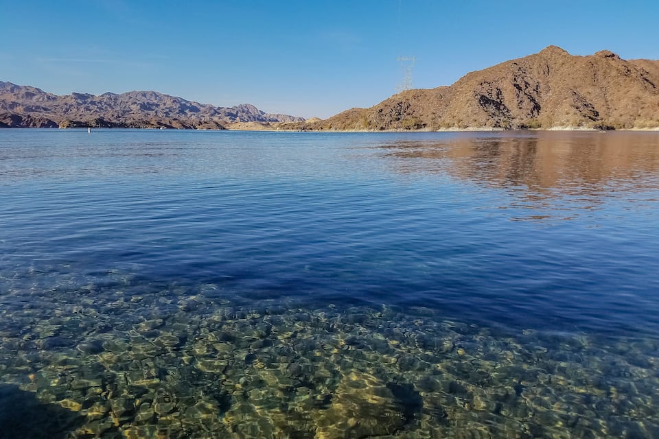 A clear lake with visible rocky bottom and mountains in the background.