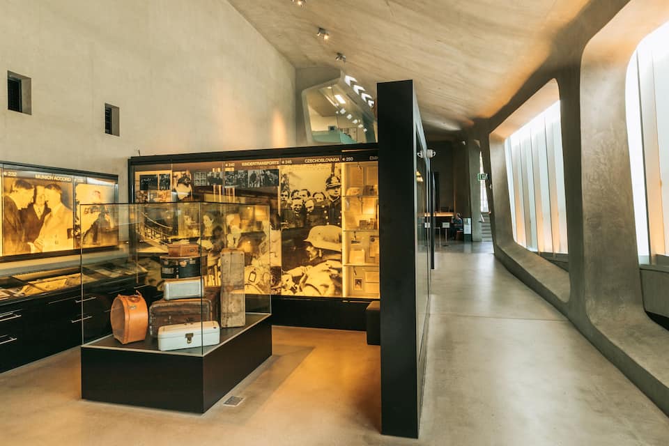 Una mostra museale con fotografie storiche e valigie d'epoca.
