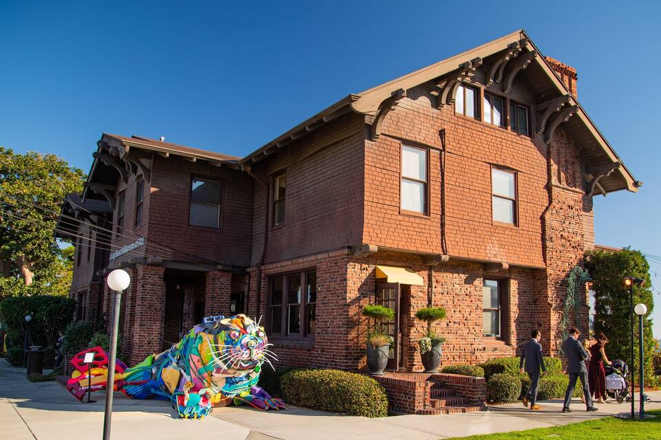 A large brick house with a gabled roof and a colorful sculpture in front.