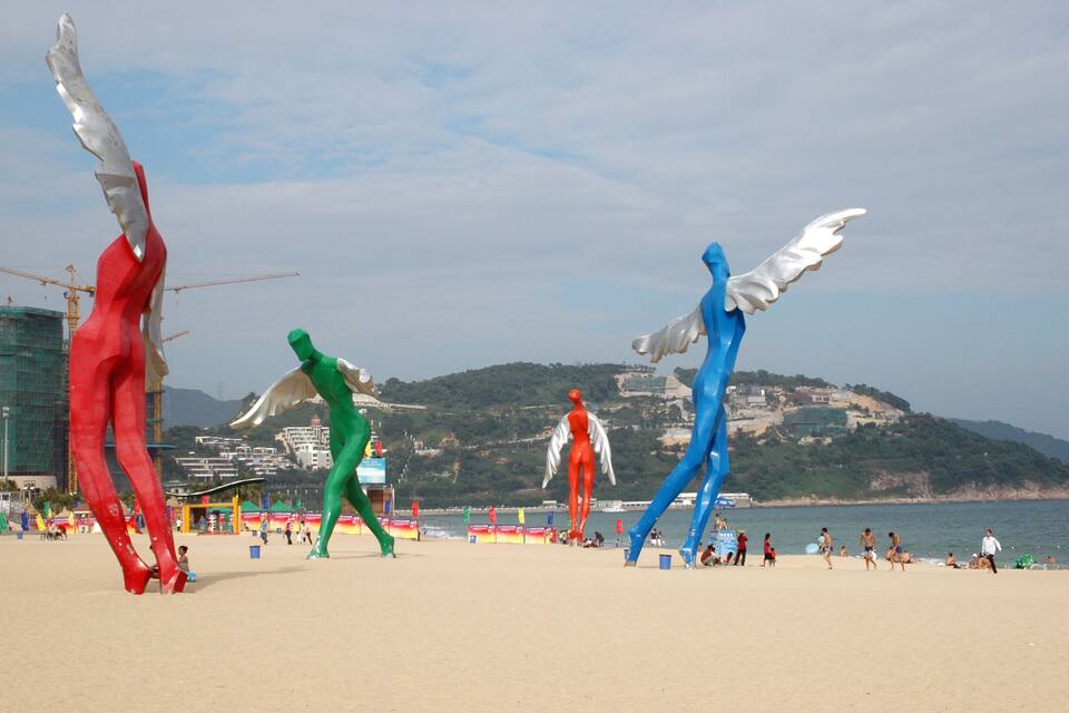 A beach with large colorful sculptures and a construction crane in the background.