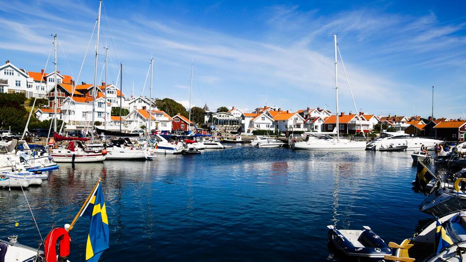 A marina with boats, houses with orange roofs, and a Swedish flag.