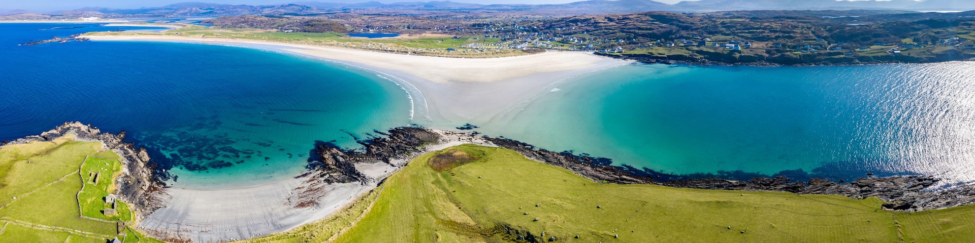 Un paysage cĂŽtier avec une plage de sable, des eaux bleues et limpides, et des champs verdoyants.