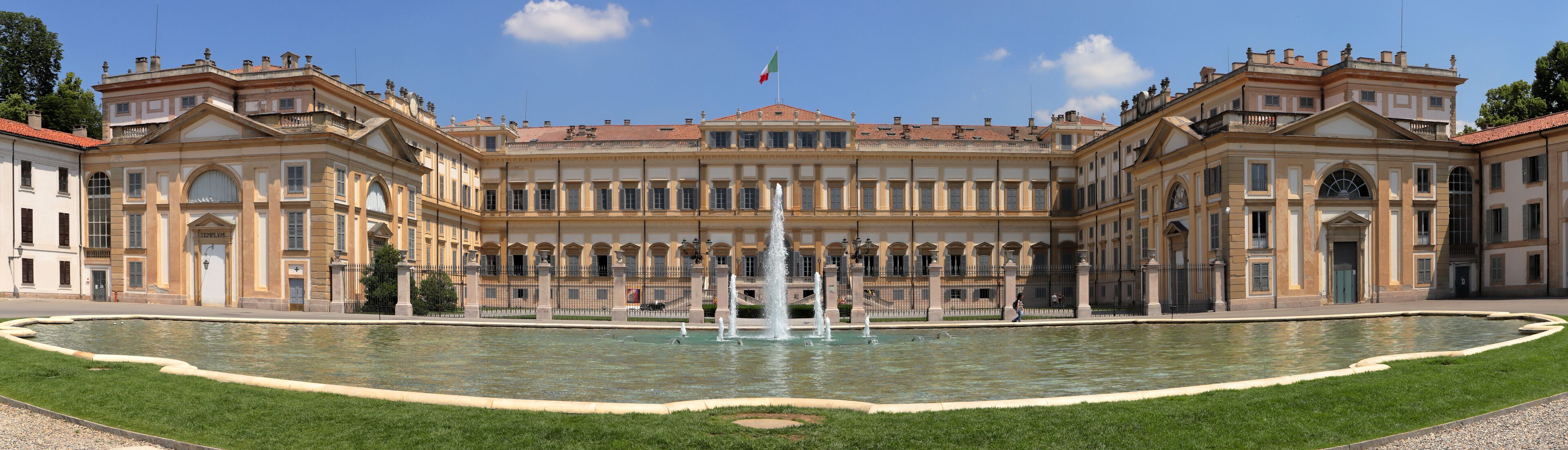 A grand classical building with a central fountain, surrounded by a well-manicured lawn.