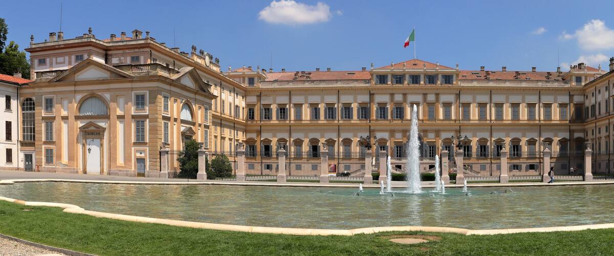 A grand classical building with a central fountain, surrounded by a well-manicured lawn.