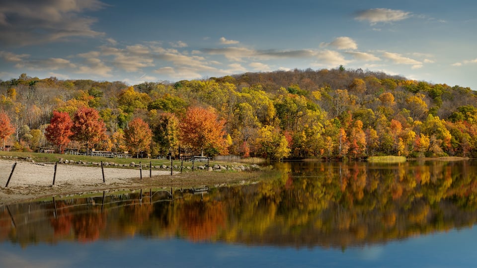 A lake reflecting autumn trees, a wooden dock, and a forested hill.