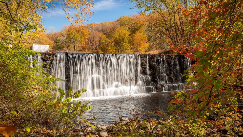 A waterfall cascading over a rocky dam surrounded by autumn foliage.