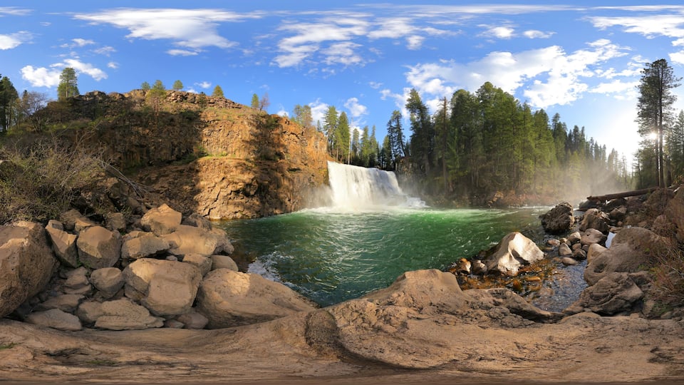 A waterfall cascading into a river surrounded by rocky terrain and dense forest.