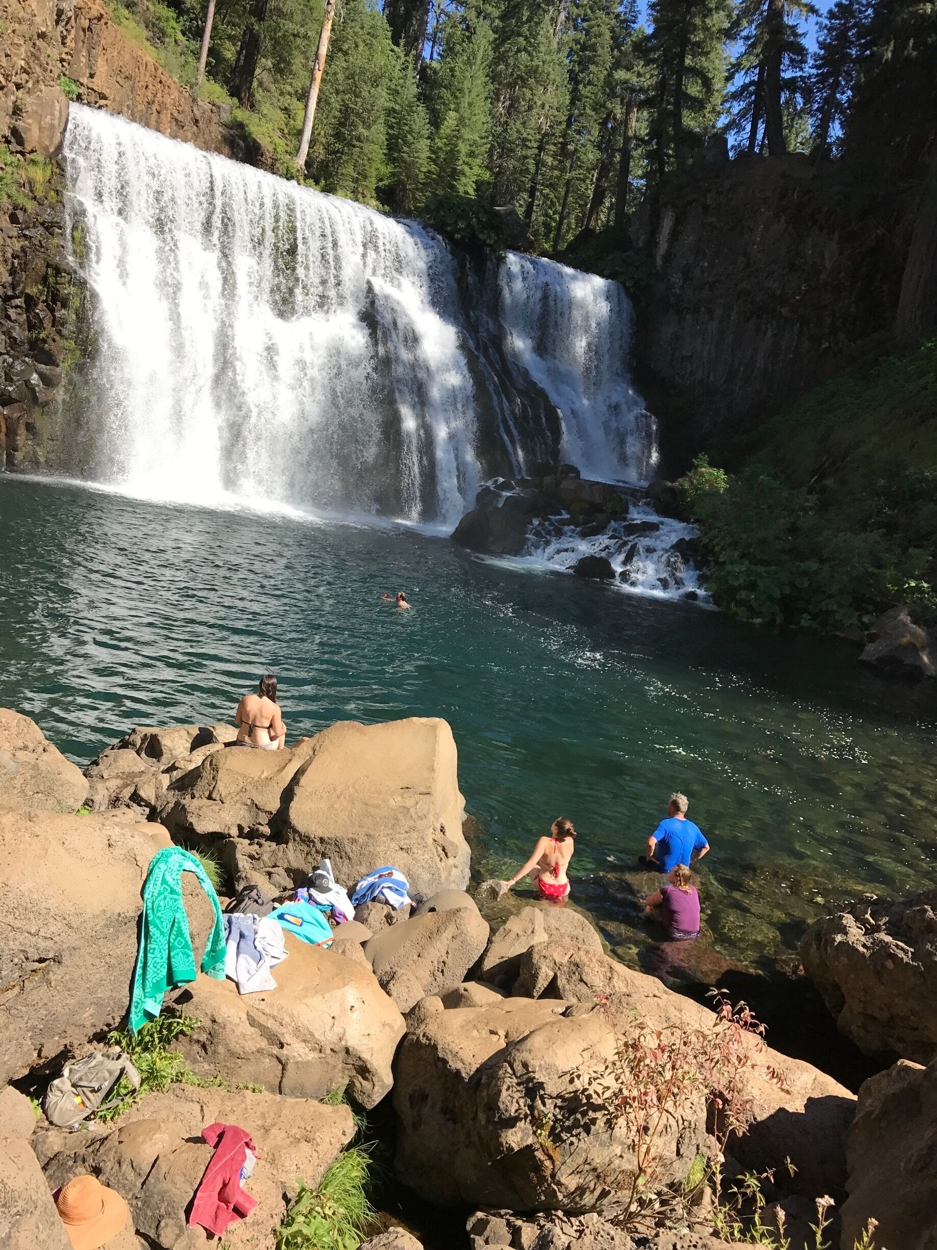 A waterfall cascading into a clear lake surrounded by rocks and trees.