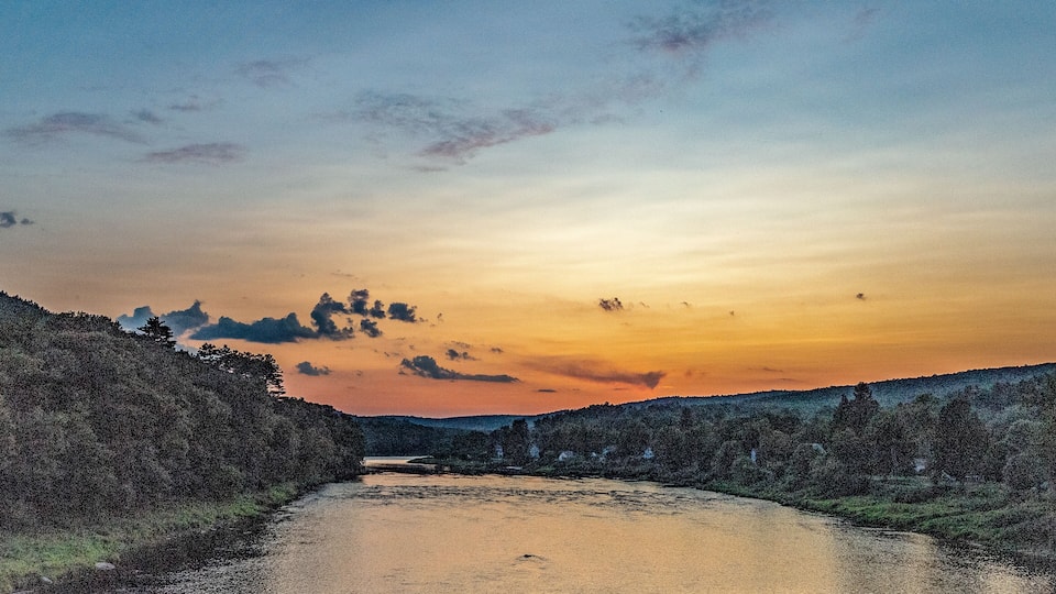 A river at sunset with a forested hillside on one side and a clear sky above.