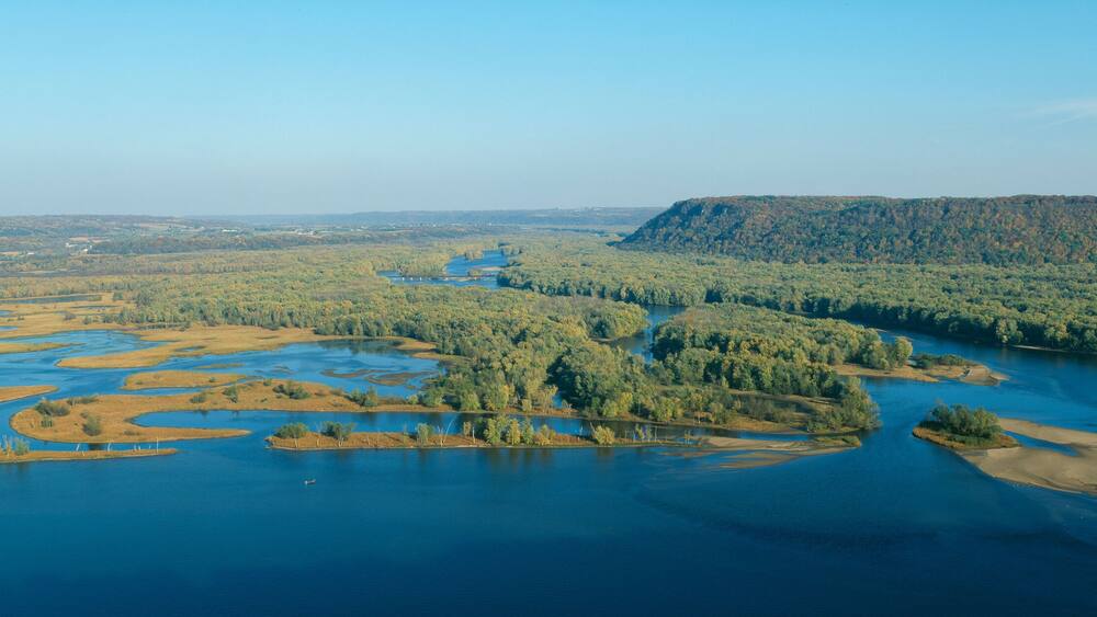 A river winding through a forested landscape with a prominent hill in the background.