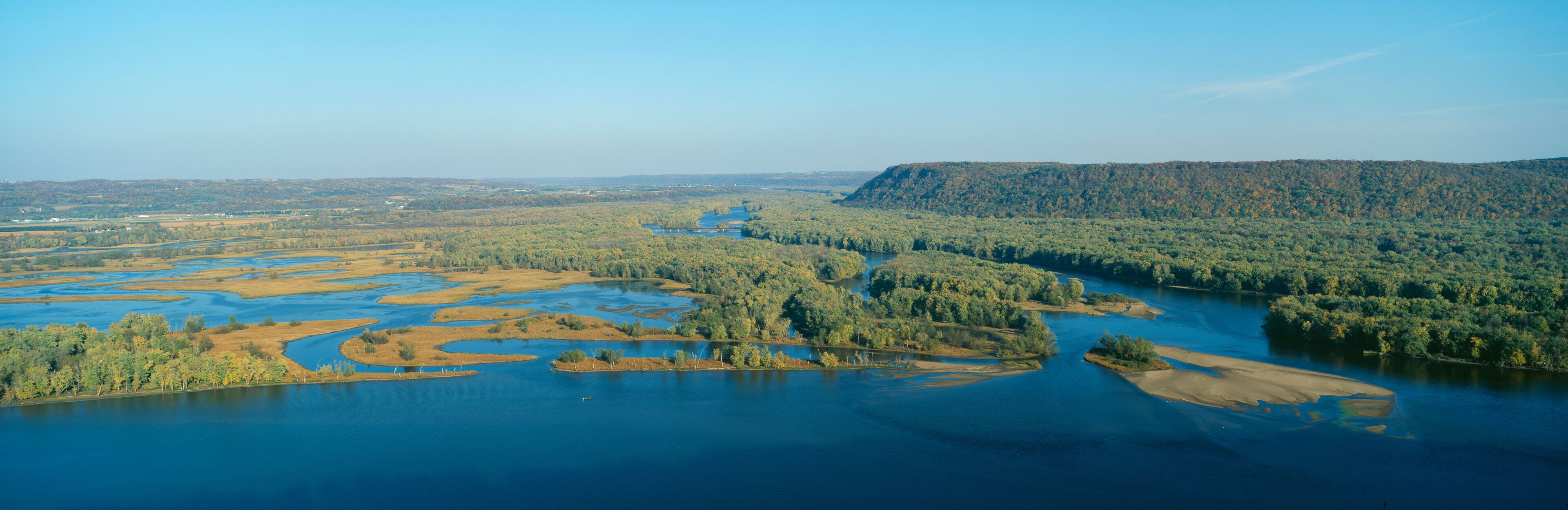 A river winding through a forested landscape with a prominent hill in the background.