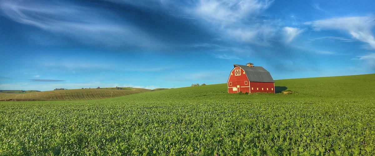 A red barn on a green field under a blue sky with clouds.