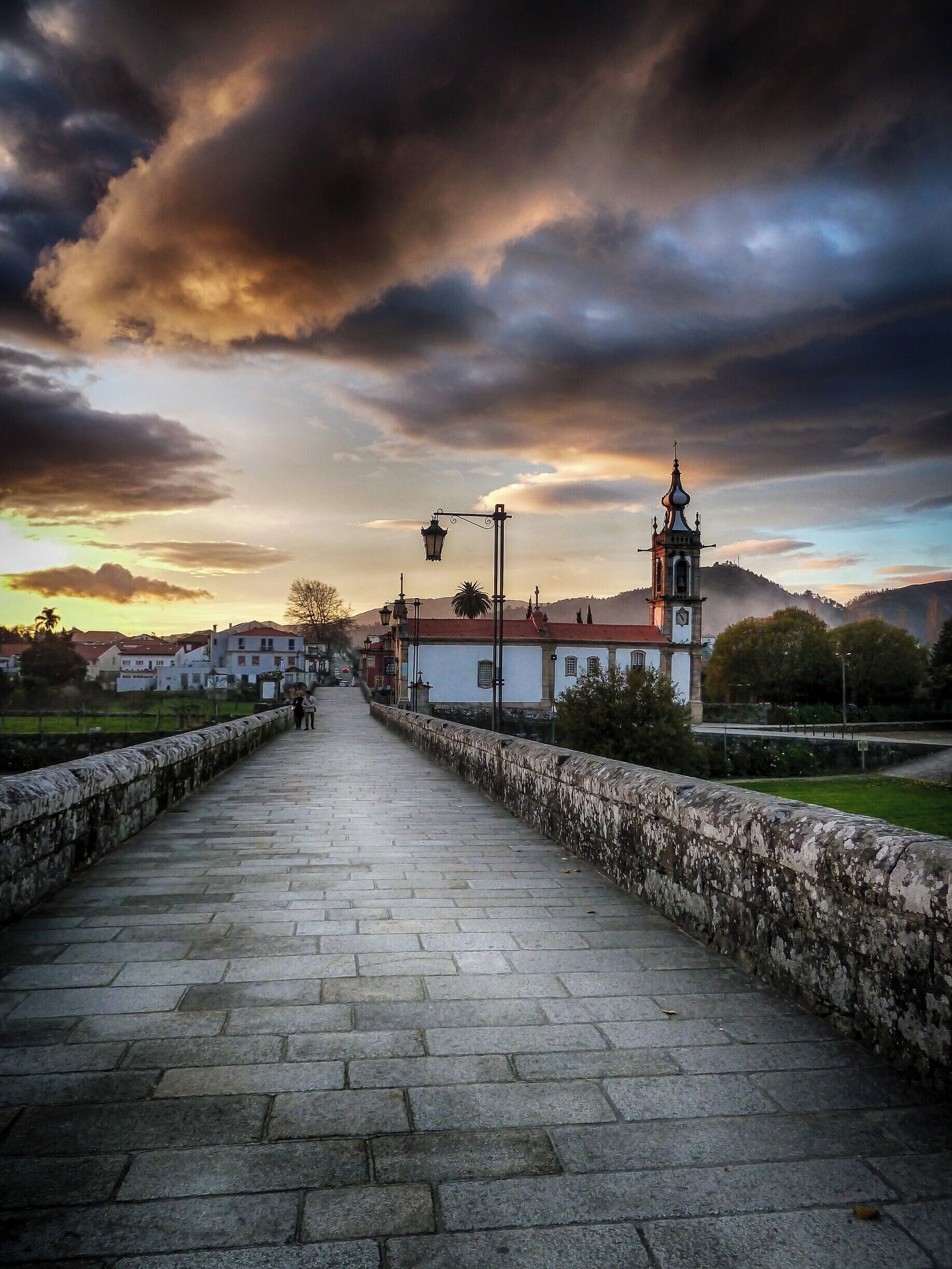 A stone bridge with a clock tower and a church in the background.