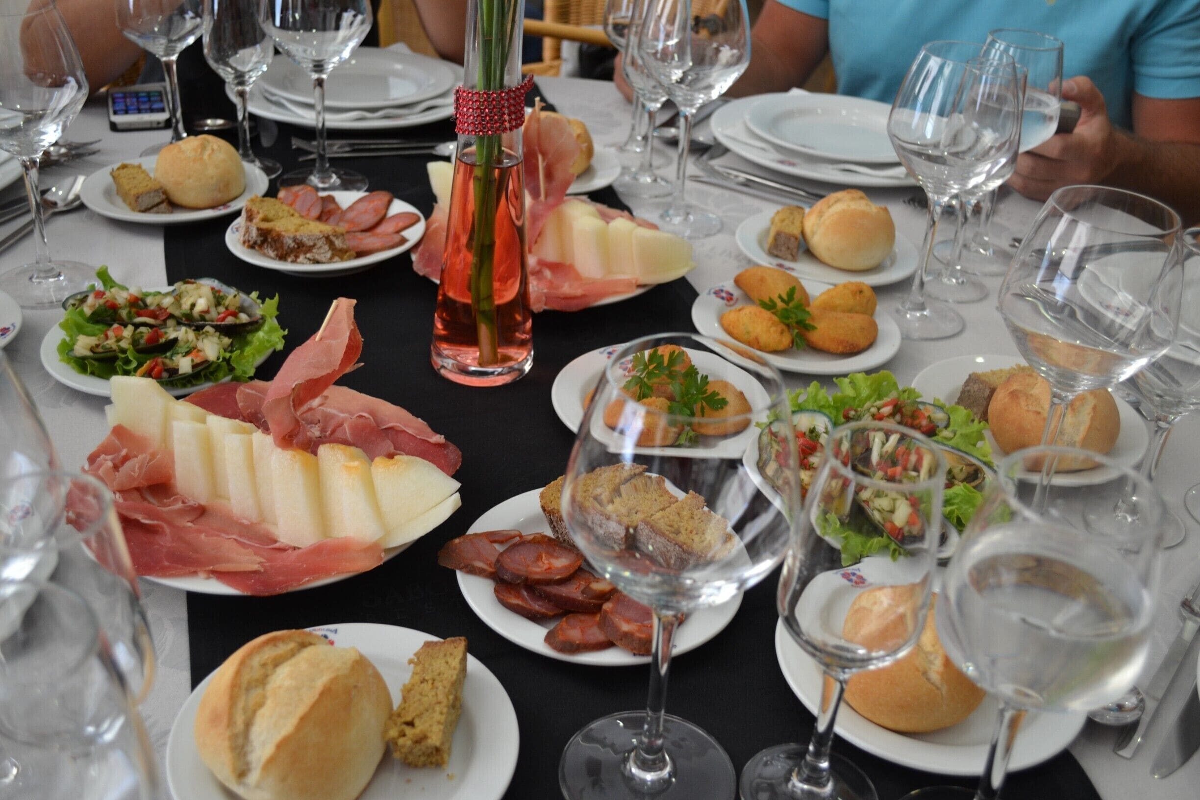 A table with various dishes, including bread, cheese, and meats, along with wine glasses and a bottle.