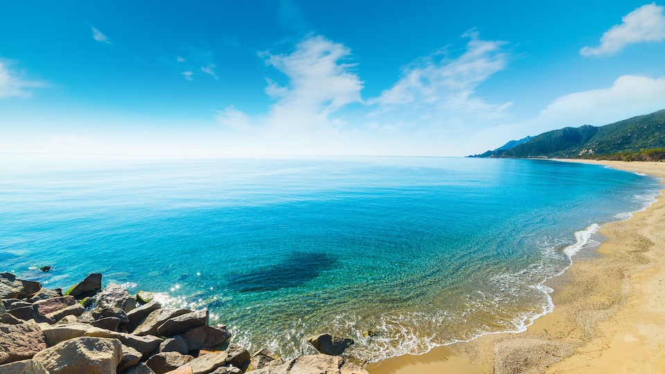 A clear blue sea, rocky shoreline, and a distant mountain range.
