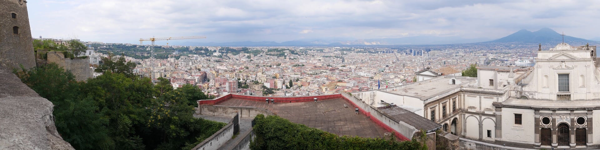 A cityscape with a view of a mountain in the distance, a construction crane, and a historic building.