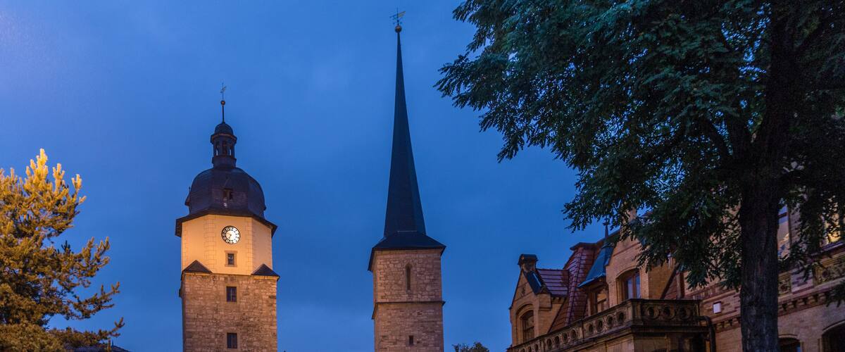 A historic town square with a prominent clock tower, a church spire, and traditional architecture.