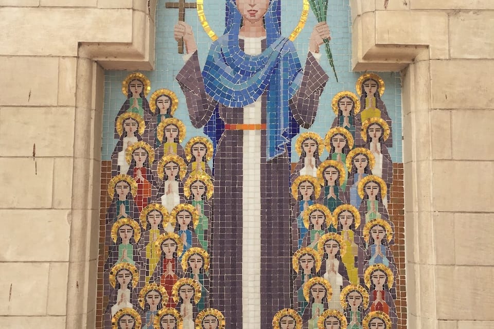 A mosaic of a religious figure holding a cross and a branch, surrounded by smaller figures with halos, set in an arched doorway.