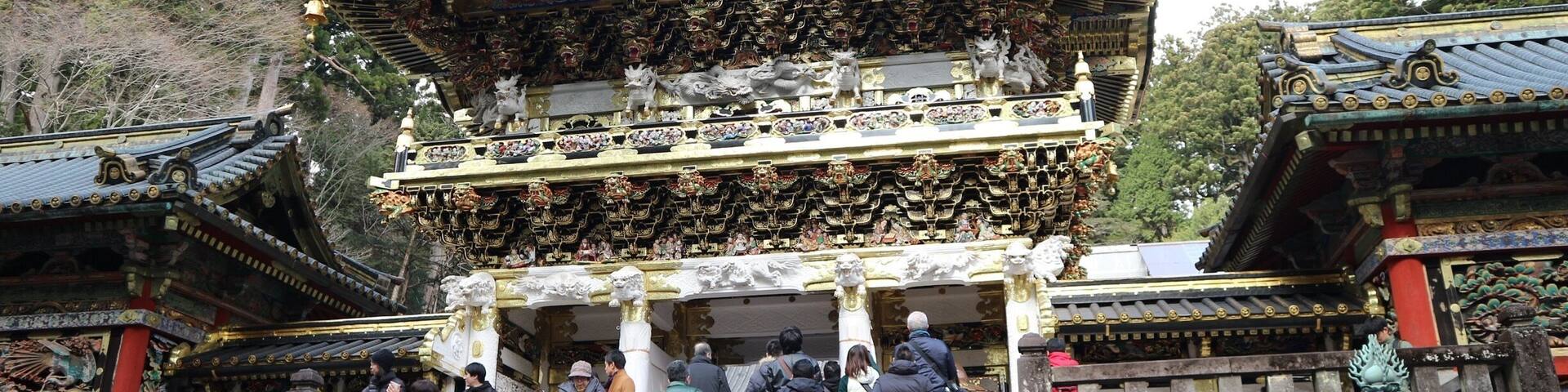 Un templo japonés tradicional con arquitectura ornamentada, una escalera que conduce a la entrada y un farol de piedra.
