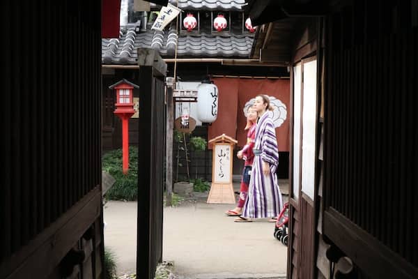 A traditional Japanese alleyway with wooden buildings, a red lantern, and a couple in traditional attire.