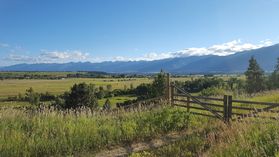 A rural landscape with a wooden fence, green fields, and distant mountains.