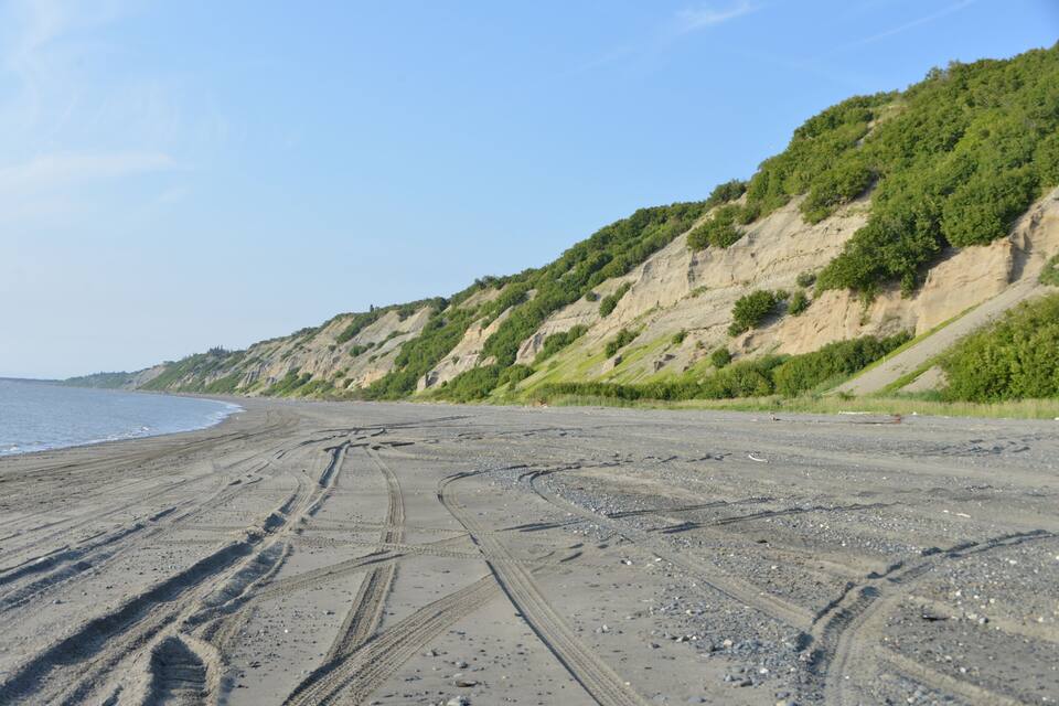 Une plage où l’on voit des traces de pneus et une côte rocheuse.