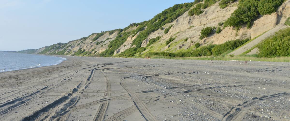 A beach with tire tracks and a rocky shoreline.