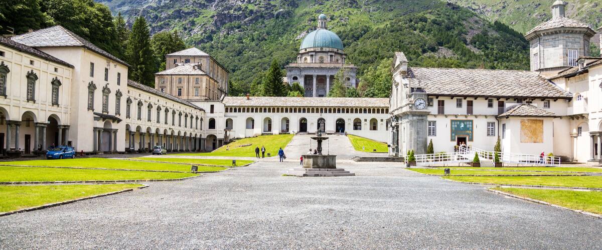 A historic courtyard with a central fountain, surrounded by classical architecture and a mountain backdrop.