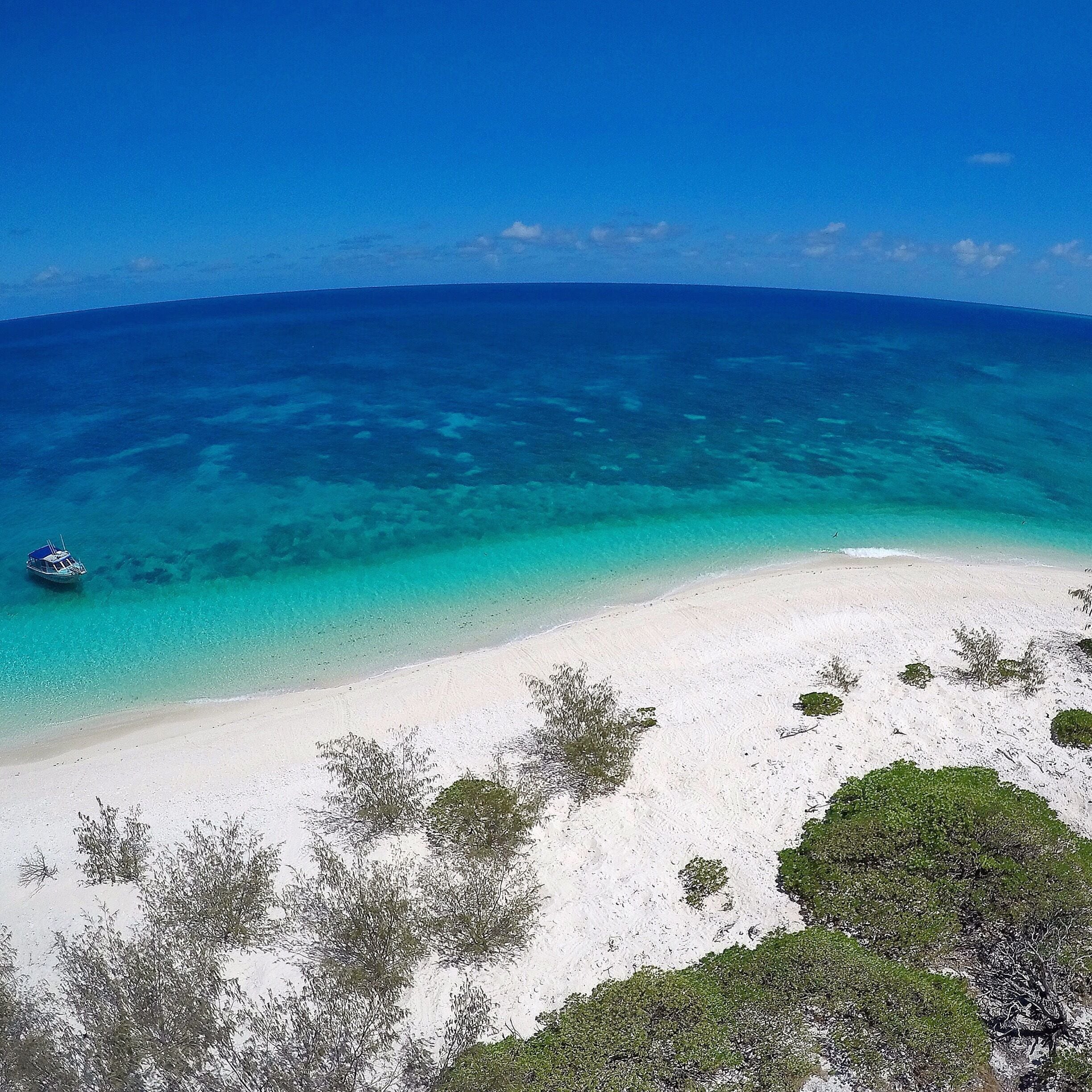 A white sandy beach with clear turquoise waters and a boat in the distance.