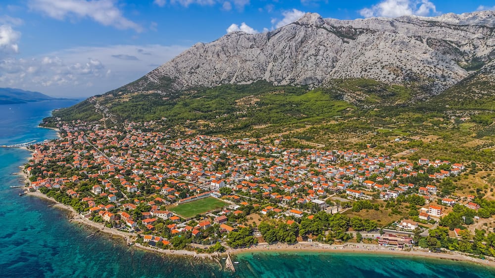 Une ville côtière aux maisons aux toits rouges, bordée par une mer d’un bleu limpide, avec une montagne en toile de fond.