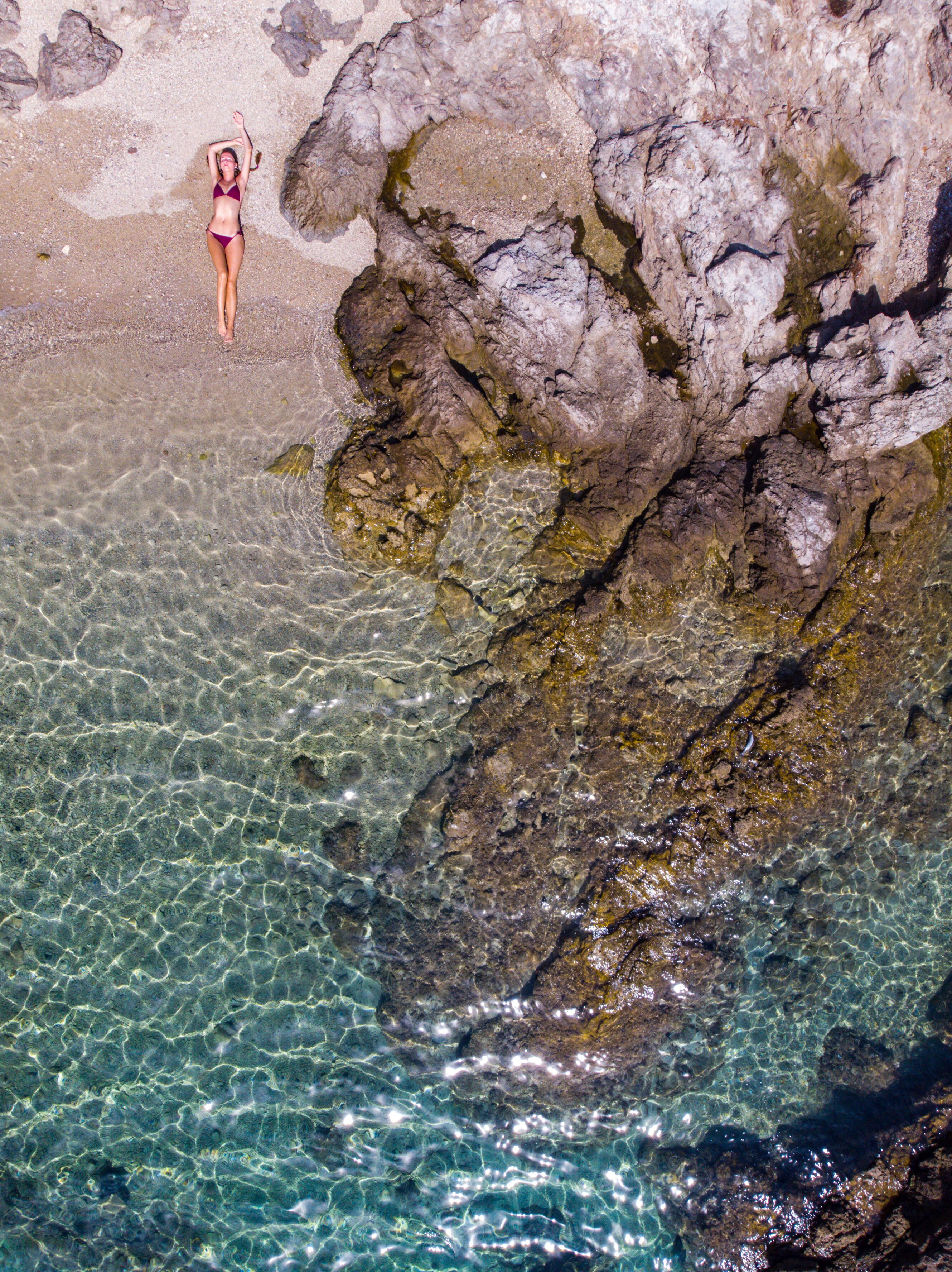 top down view of a girl in a bikini lying on the sand on the seashore; relaxing on a paradise beach as seen from a drone; a beautiful model lying on the sand
