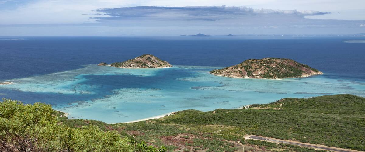 A coastal landscape with two prominent hills and a clear blue sea.